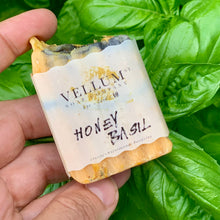 Load image into Gallery viewer,
Hand holding a bar of Vellum Soap Company Honey Basil soap against a green leafy background