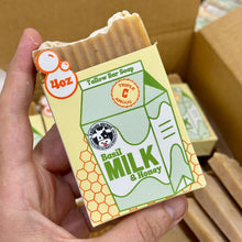 Load image into Gallery viewer, Bar of Bail Milk &amp; Honey Tallow soap with a label held by a hand, set against a cardboard box background.
